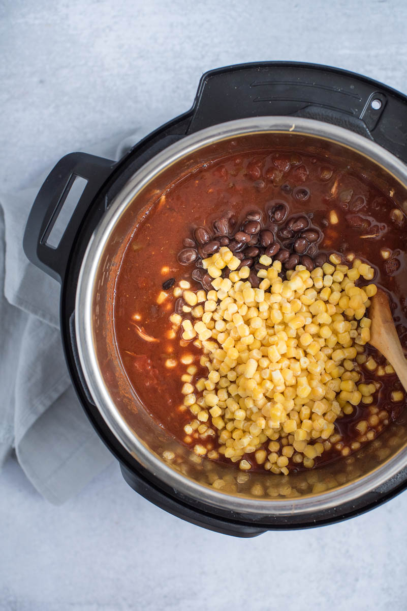 Adding the corn and beans to chicken enchilada soup made in an Instant Pot.