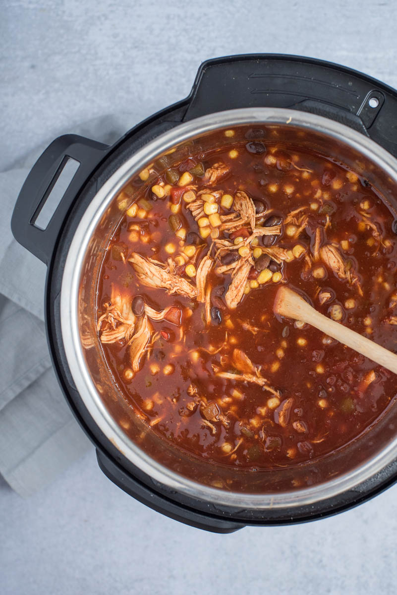 Chicken enchilada soup cooked in an Instant Pot with a wooden spoon for storing.