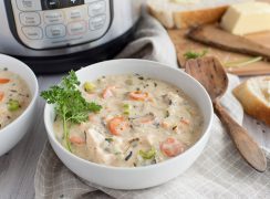 White bowl of creamy pressure cooker chicken wild rice soup garnished with parsley in front of an Instant Pot with white bread and a wooden spoon.