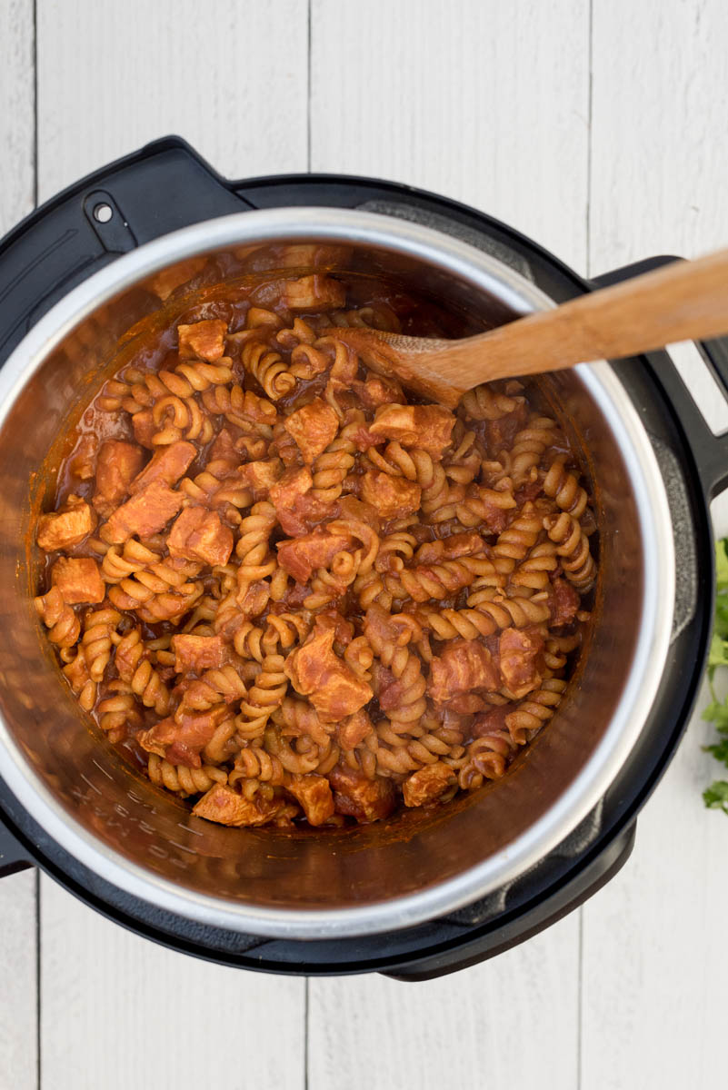 Overhead picture of chicken enchilada pasta cooked in an Instant Pot with a wooden spoon used for stirring.