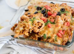 Instant Pot chicken enchilada pasta being scooped from a serving dish using a wooden spoon.