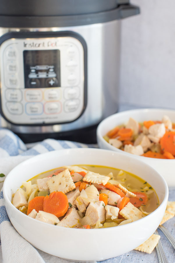 Best Pressure cooker chicken noodle soup dished up in a white serving bowl with a second bowl and an Instant Pot in the background.