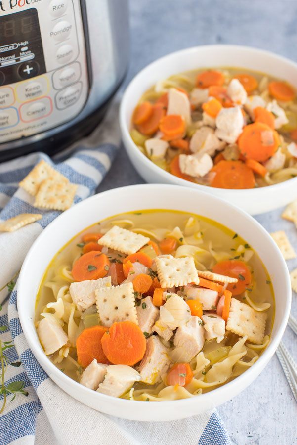 pressure cooker chicken soup recipe served in two white bowls in front of an Instant Pot