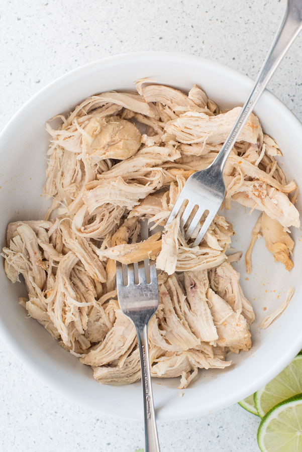 A bowl of pressure cooker chicken taco filling being shredded with two forks.