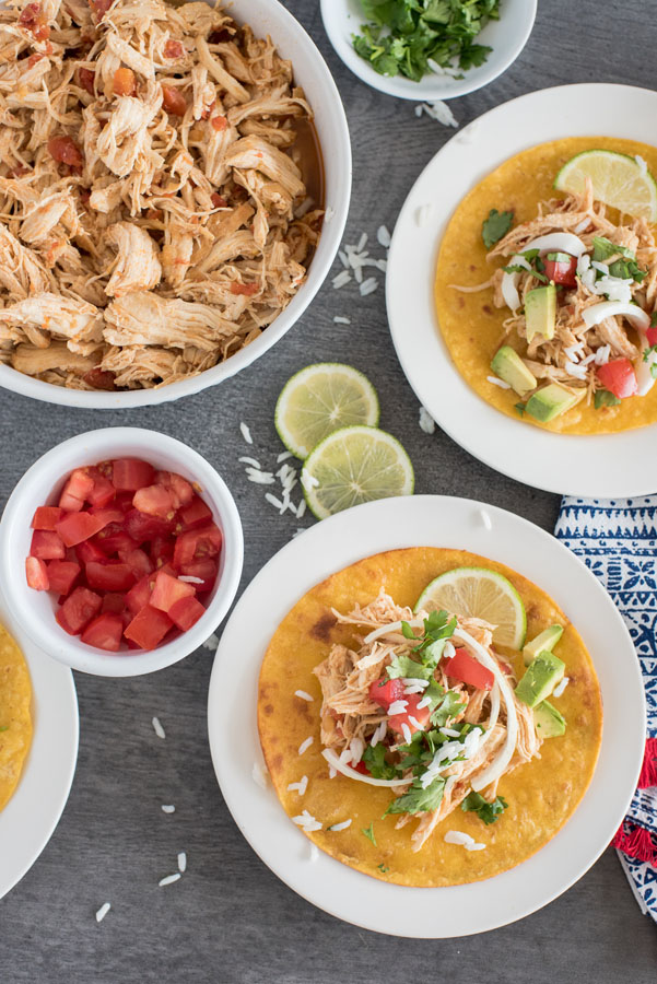 An overhead shot of shredded chicken tacos pressure cooker, with diced tomatoes, cilantro, limes, and additional Instant Pot shredded chicken taco filling