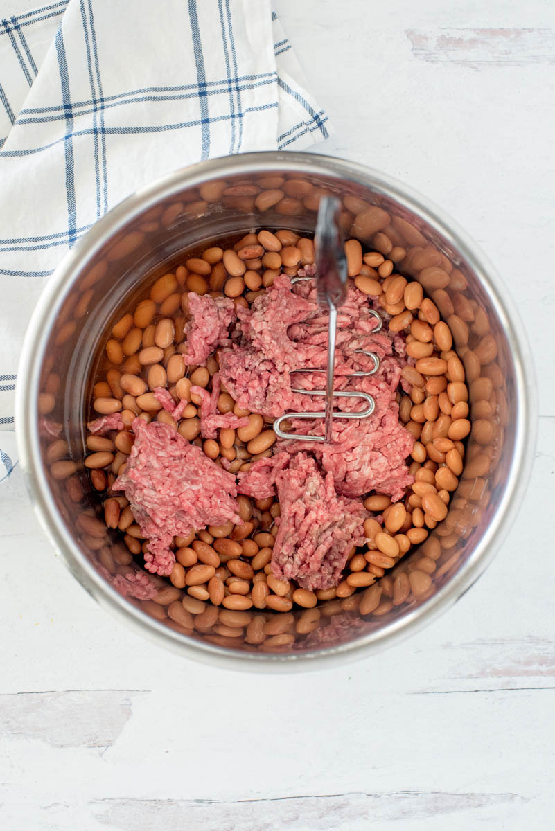 overhead of an instant pot mashing ground beef and cooked beans