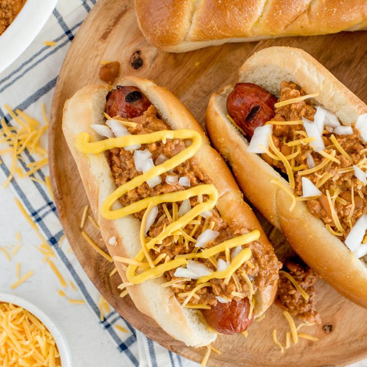 Overhead close up shot of two hot dogs topped with Instant Pot chili dog sauce, garnished with mustard, onions, and cheese