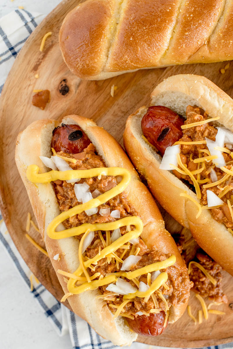 two hot dogs in buns with chili, cheese and mustard on top