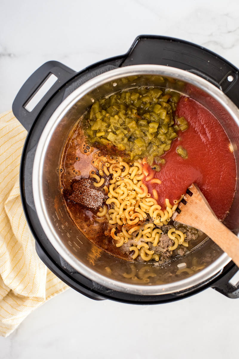 An overhead shot looking into an Instant Pot filled with macaroni, sausage, diced green chiles, and tomato sauce
