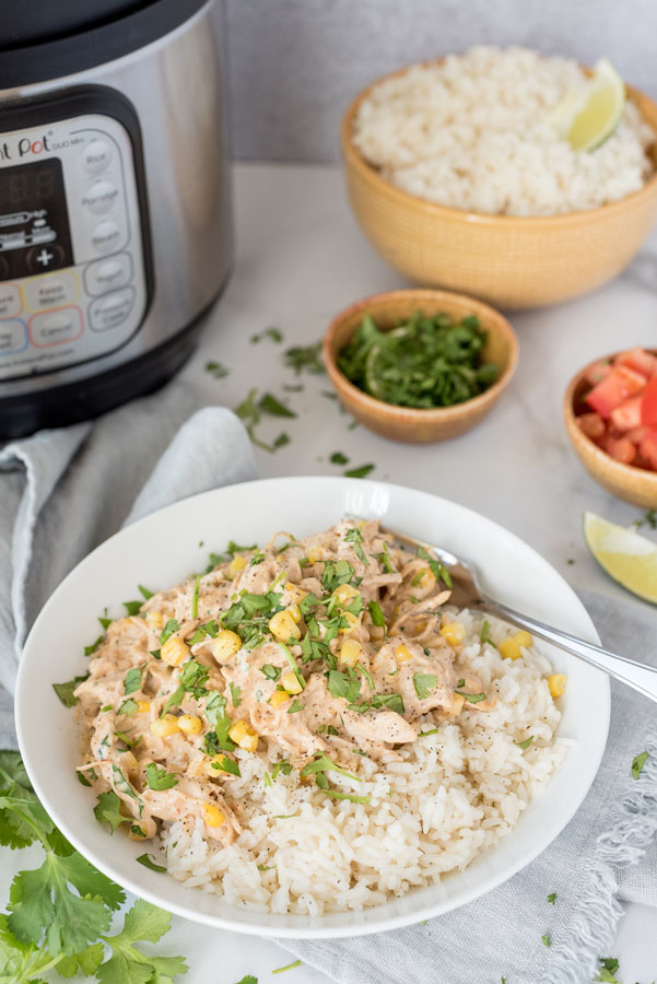 Overhead image of creamy chipotle chicken served over white rice, and garnished with cilantro, served in a white bowl and set in front of an Instant Pot.
