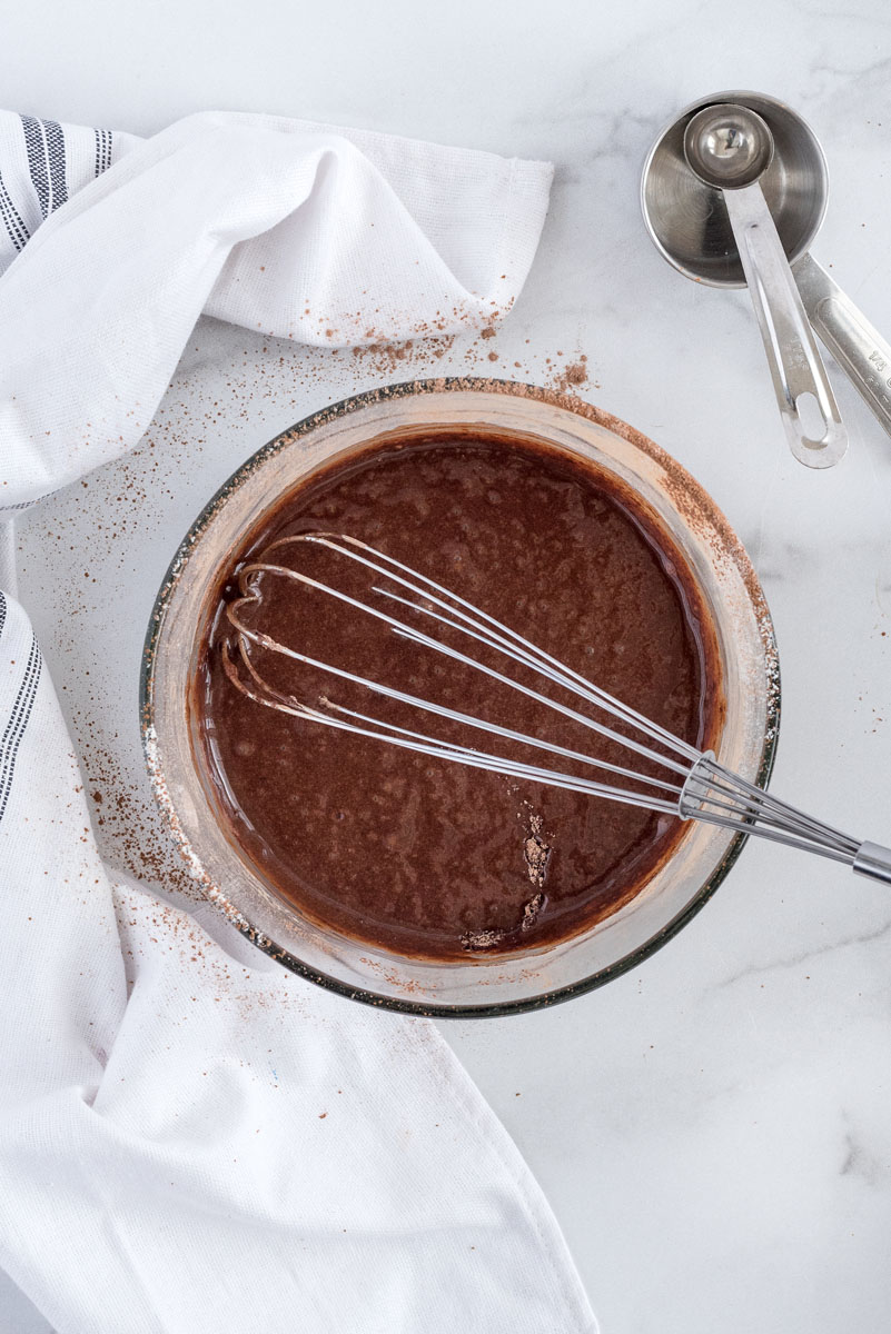 batter for chocoalte cake for two in a glass mixing bowl with a wire whisk