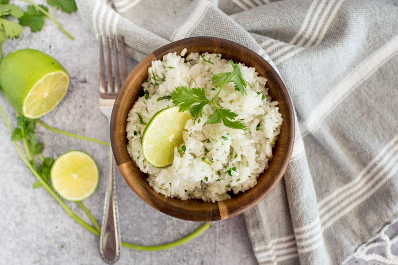 Instant Pot Cilantro ime Rice in a brown wooden bowl with a grey background and fresh lime and cilantro for garnish
