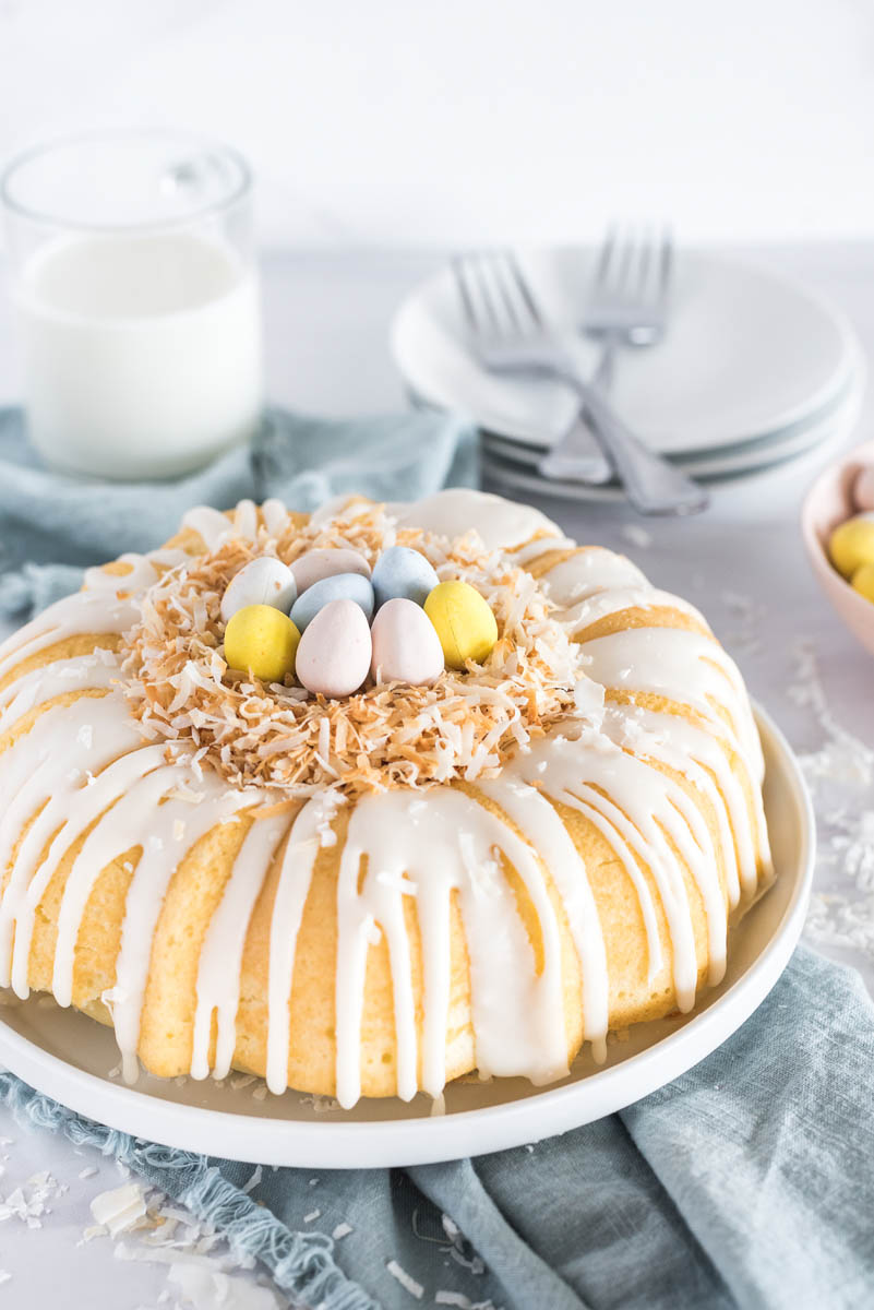 Coconut cake with the birds nest decoration in place on top, with a glass of milk and white plates and forks visible in the background