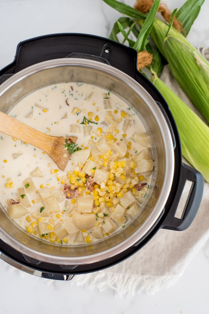 cooking instant pot corn chowder in an electric pressure cooker with a wooden spoon
