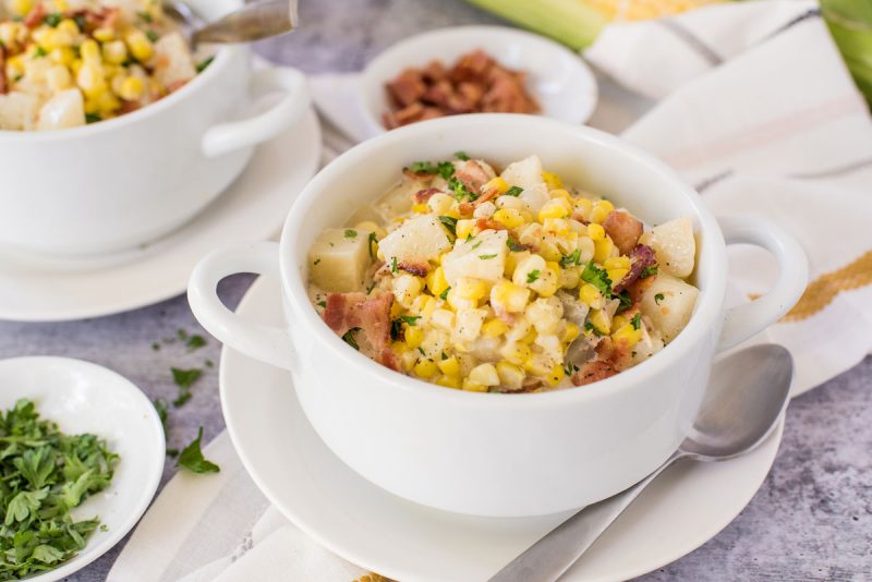 bowl of instant pot corn chowder with fresh corn on the cob and bacon