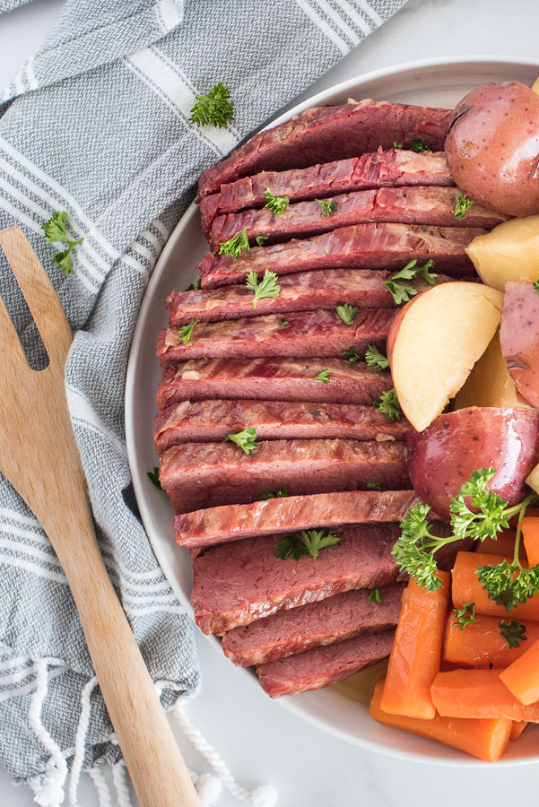 Close up overhead of Instant Pot Corned Beef and Cabbage for St. Patrick’s Day on a whtie serving platter with a white and grey linen napkin.