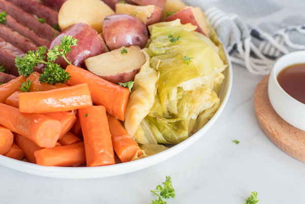 close up of tender cabbage, carrots and potatoes made in the pressure cooker / Instant pot on a white serving dish with flavorful beef sauce on the side.