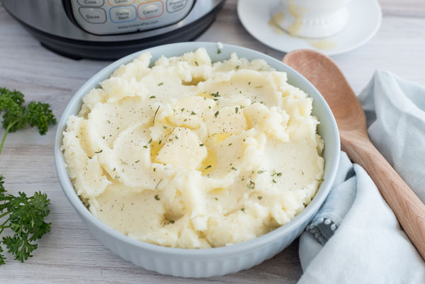 Instant Pot Creamy Mashed Potatoes, dished in a serving bowl with a wooden spoon sitting on the side
