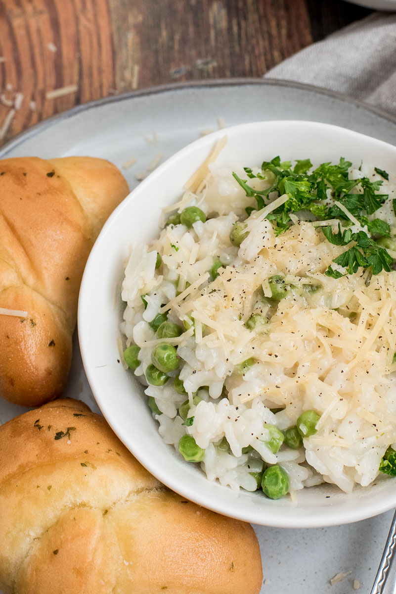 Close of of lemon risotto made in and Instant Pot with peas, parmesan, and fresh parsley next to some rolls.