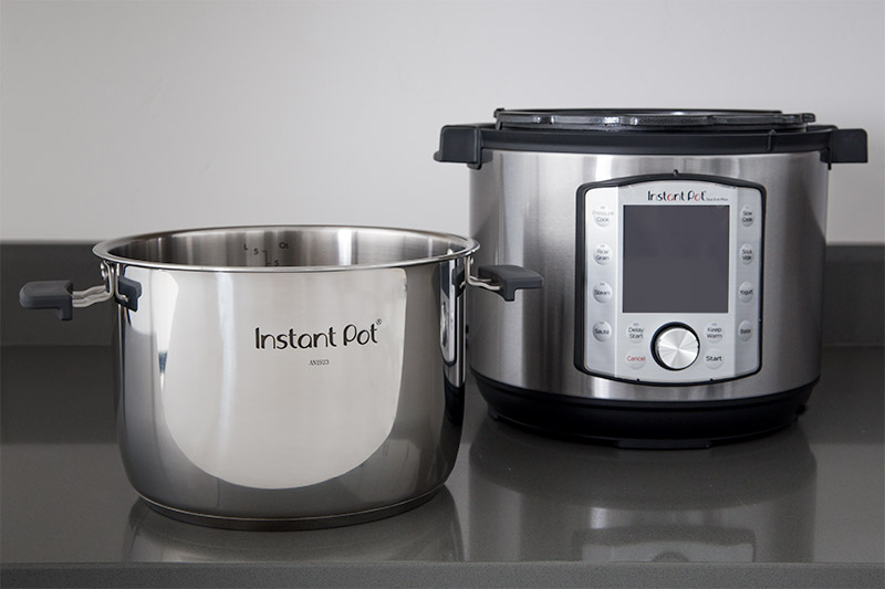 Instant Pot Evo inner pot with handles next to pressure cooker housing.