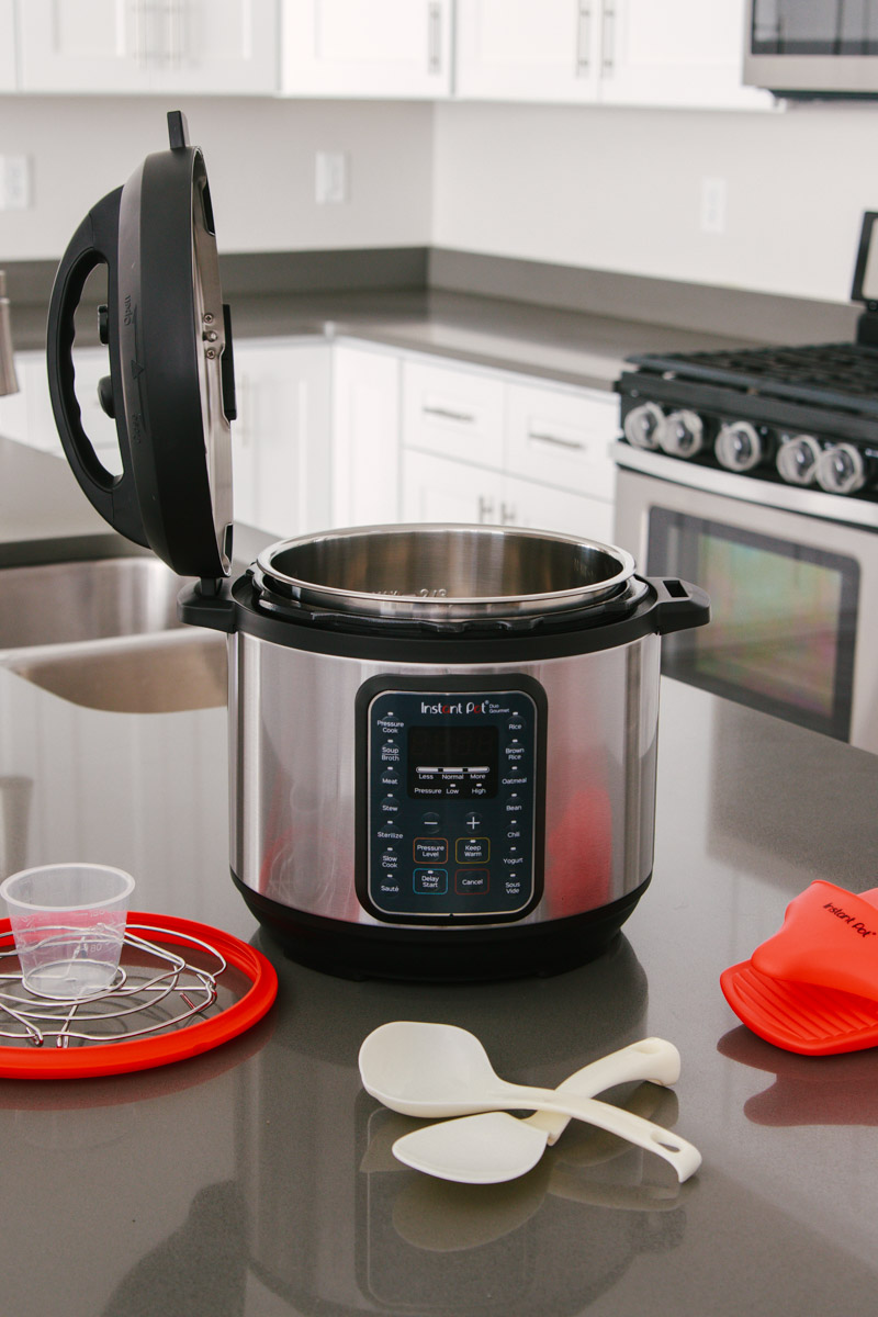 45 degree shot of the Instant Pot Duo Gourmet with the lid resting upright in the lid fin slot, surrounded by the accessories that come with it on a gray countertop