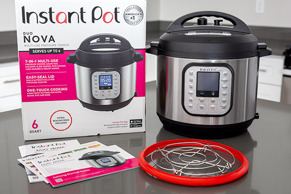 Instant Pot Duo Nova shown with provided accessories including extra sealing ring, trivet that can fold flat, getting started guide, and cooking times diagram.