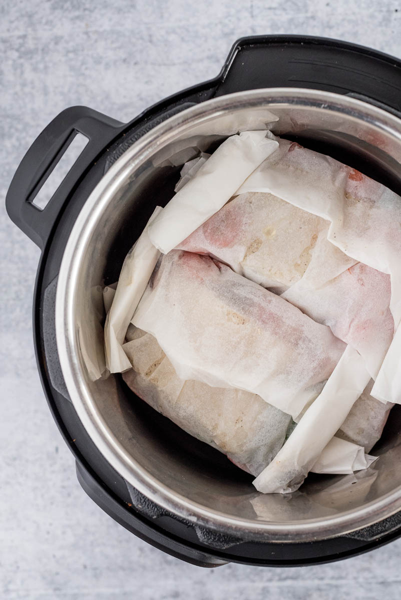 overhead of an instant pot with two parchment packets of fish inside