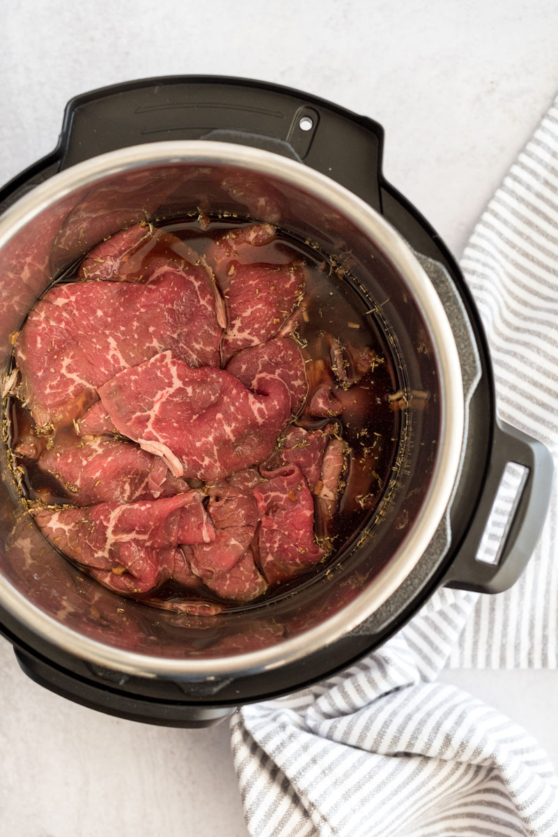 Sliced beef for French dip sandwiches ready to cook inside an Instant Pot.