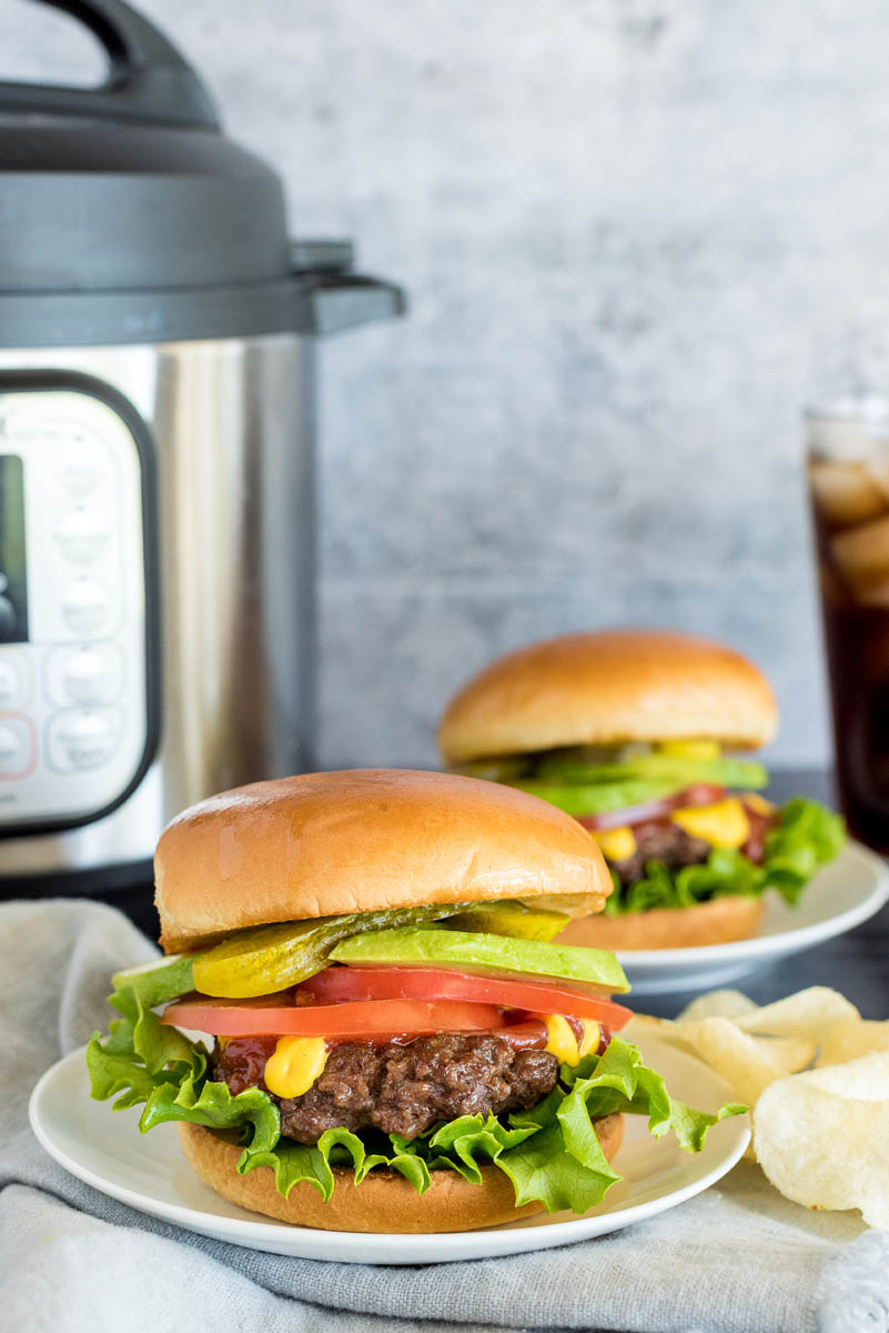two onion burgers with toppings in front of an instant pot pressure cooker