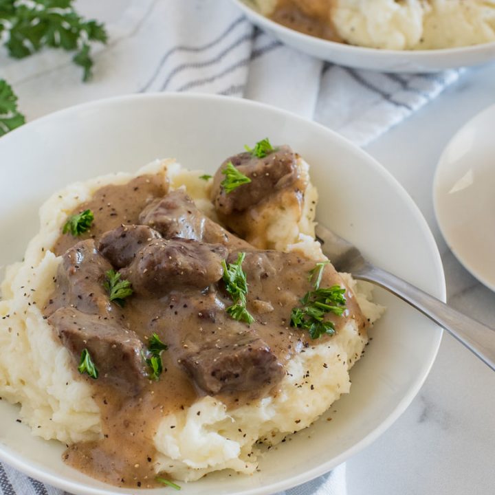 serving of swedish beef stew over mashed potatoes in a white bowl