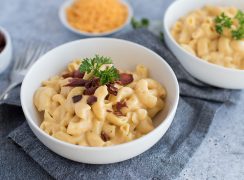 Two bowls of homemade pressure cooker macaroni and cheese topped with fresh parsley and crumbly bacon with a bowl of shredded cheddar cheese in the background.