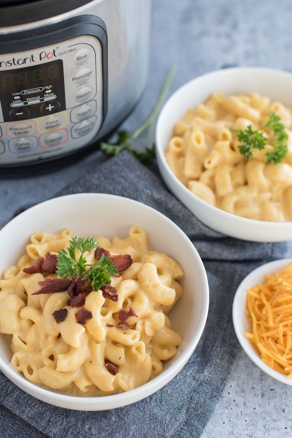 Overhead of two bowls of homemade macaroni and cheese with an Instant Pot and a bowl of shredded sharp cheddar cheese.