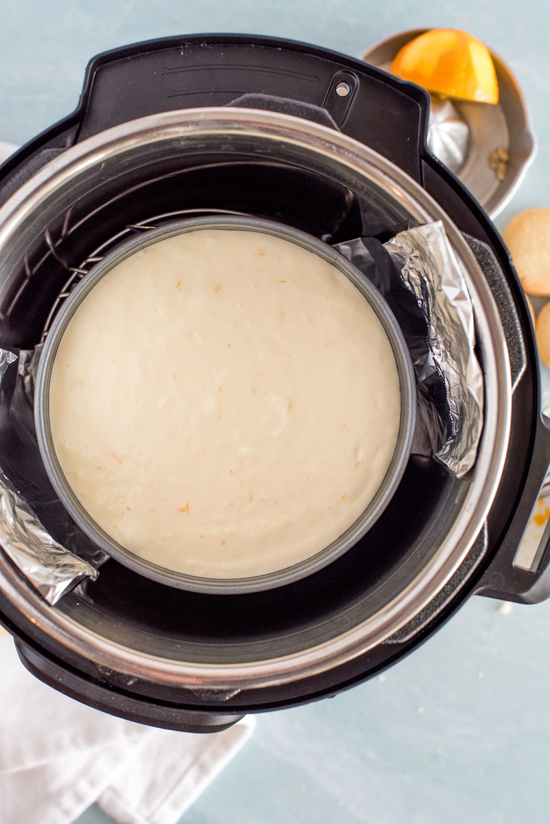lowering an instant pot cheesecake into the pressure cooker with a foil sling