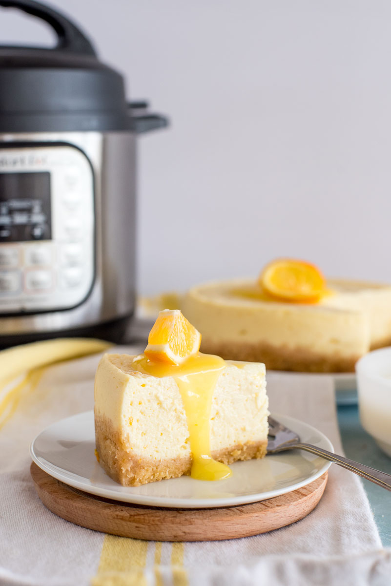 instant pot with a slice of lemon cheesecake in front on a plate