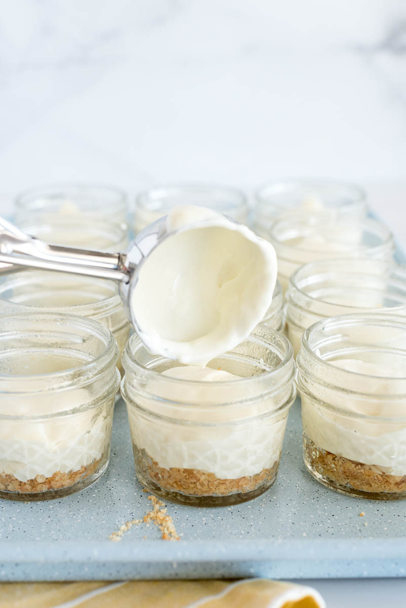 Close-up of a 45 degree shot using a disher to scoop the cheesecake batter into the mini mason jar cheesecakes