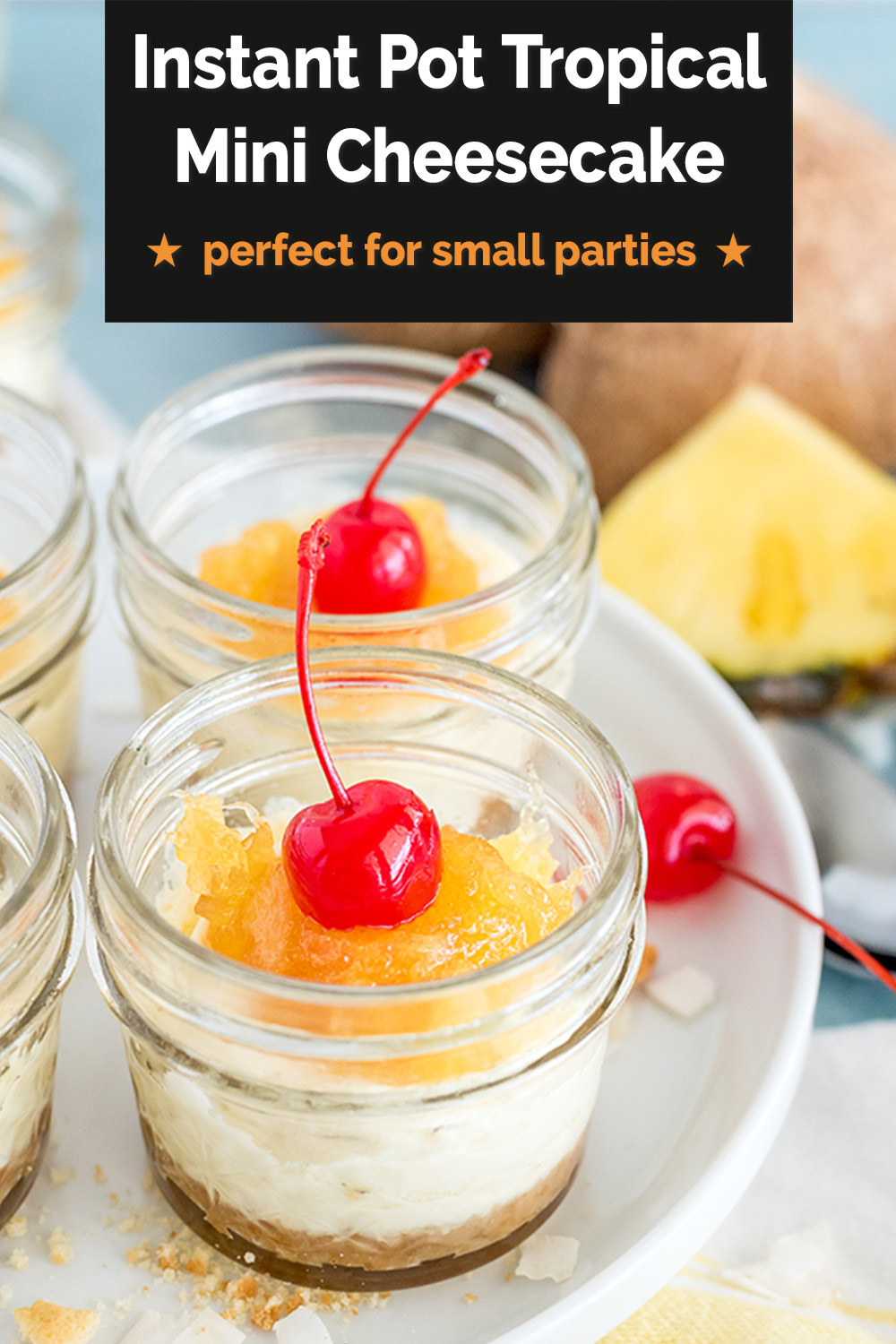A Pinterest image that reads "Instant Pot Tropical Mini Cheesecakes: perfect for small parties" overlaid on a close-up image of two mini mason jars filled with coconut cheesecake, pineapple topping, and a maraschino cherry with a pineapple wedge and a coconut in the background via @PressureCook2da