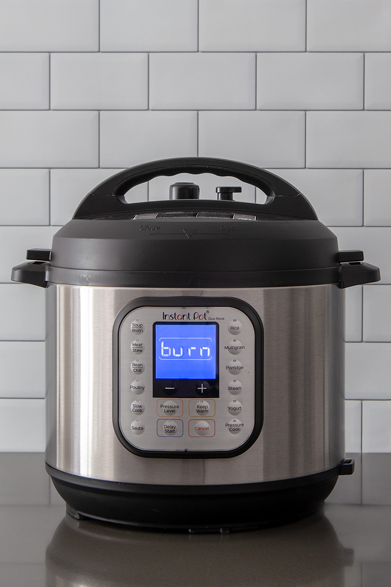 A tight, head-on vertical shot of an Instant Pot Duo Nova on a gray counter displaying the burn warning on a blue digital screen