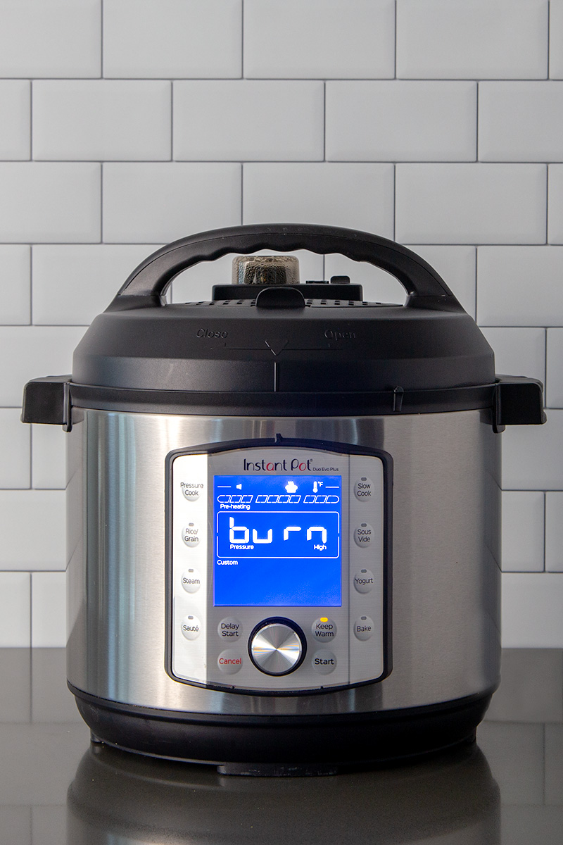 A tight vertical shot of an Instant Pot Duo Evo Plus showing a burn message on a gray counter and a white subway tile background