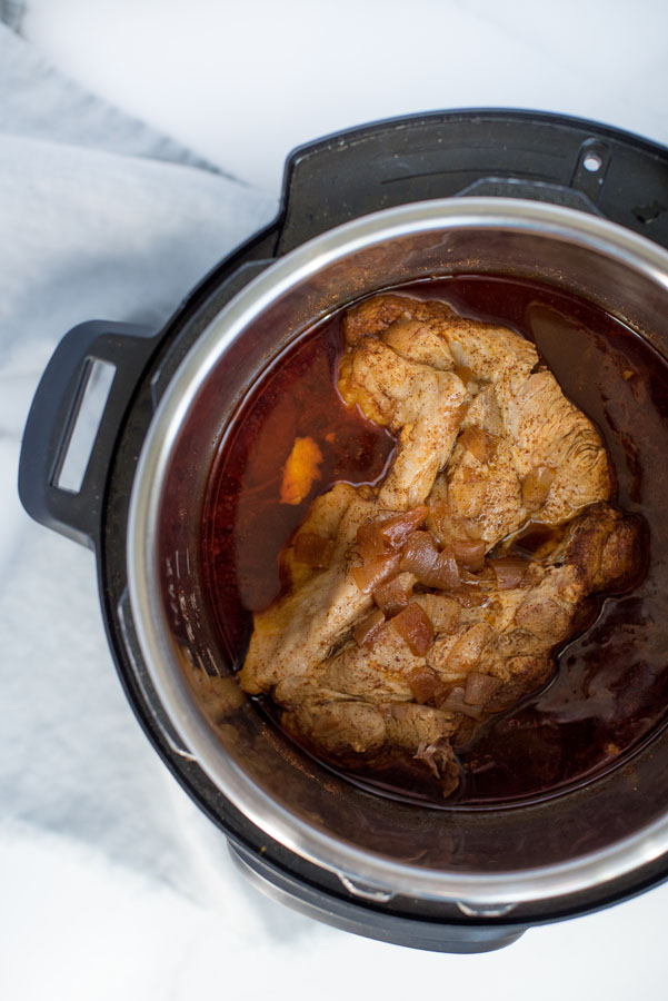 Overhead of boneless pork shoulder in an electric pressure cooker / Instant pot with seasonings to make shredded pork to fill homemade pork tamales. 