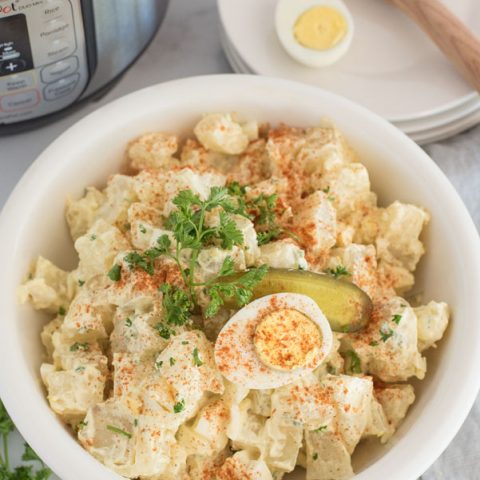 pressure cooker quick potato salad with hard boiled eggs in front of an instant pot with a wooden spoon in the background