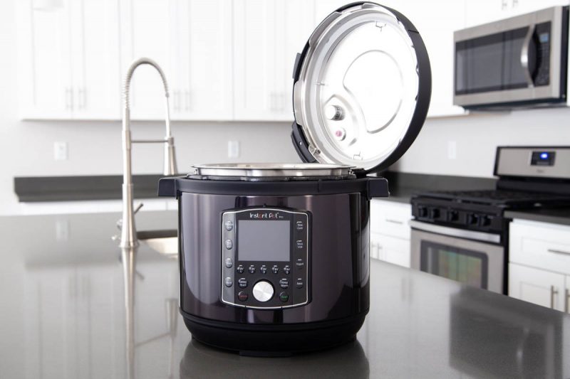 Instant Pot Pro in black stainless steel in a gray kitchen with white cabinets, with the pressure cooking lid resting in the lid fins