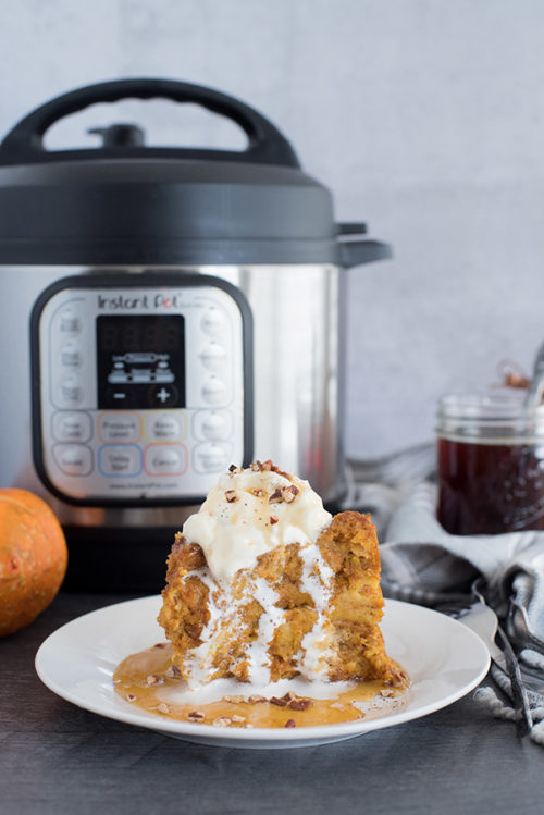 Instant Pot Pumpkin Spice Baked French Toast with whipped cream and pecans on top. Instant pot and maple syrup in the background
