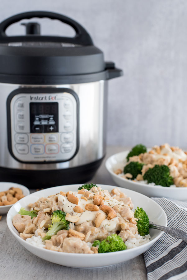 45 degree shot of a rosemary cashew chicken in a bowl with rice, cashews, and broccoli. Set in front of an Instant Pot.