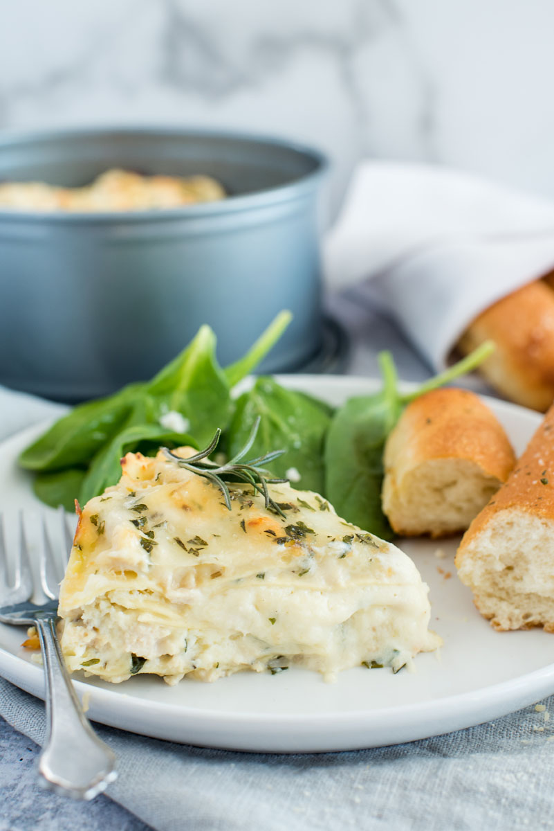 Instant pot white chicken lasagna on a white plate with a bread stick and greens