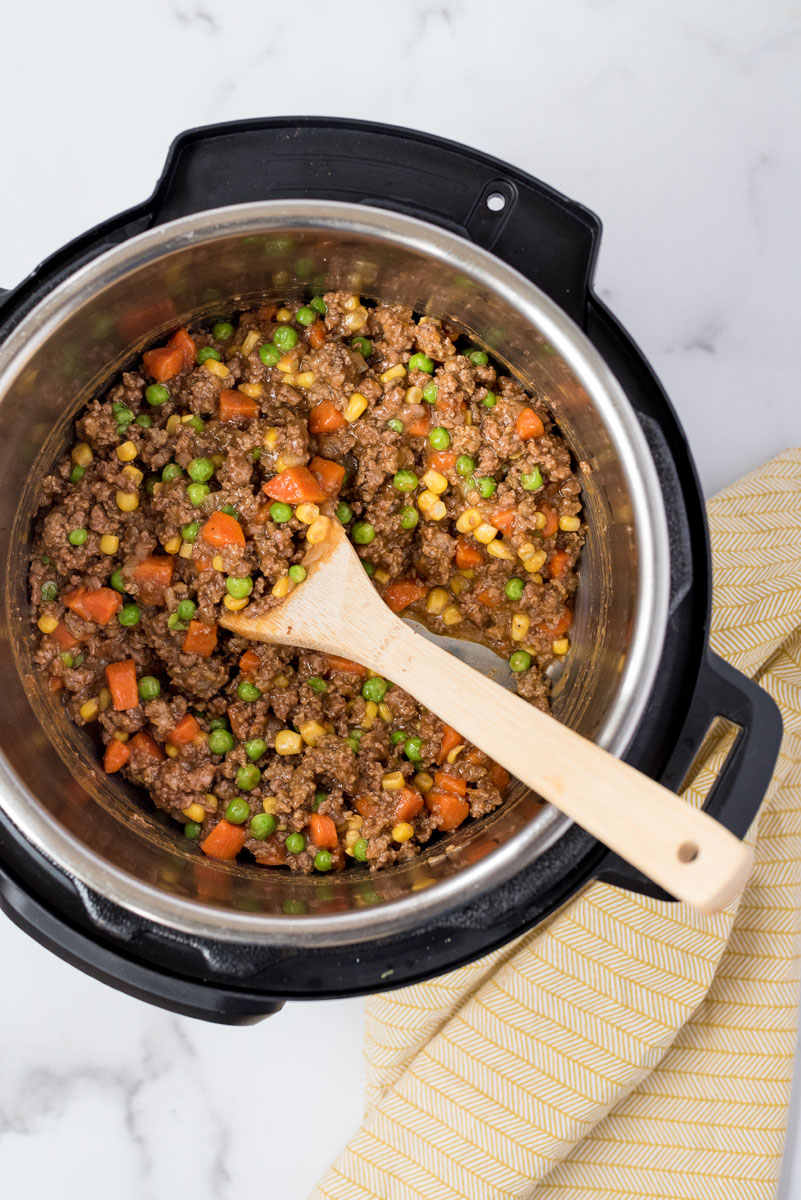 Meat mixture for pressure cooker shepherds pie cooking in an Instant Pot with a wooden spoon.