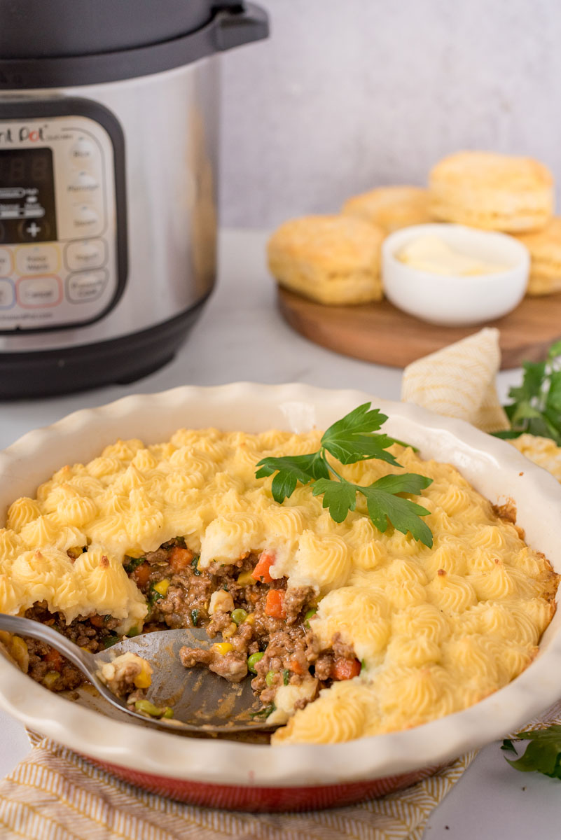 Shepherds pie made in an Instant Pot scooped out of the serving dish and placed in front of biscuits and an Instant Pot.