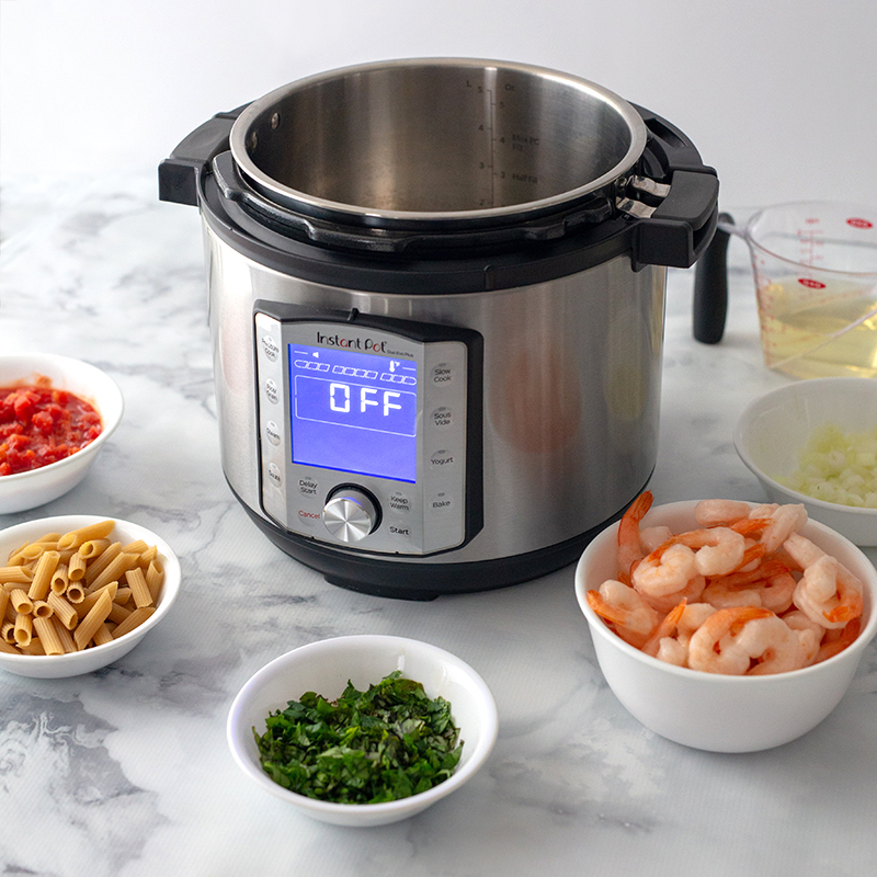 Diced tomatoes, penne pasta, chopped basil, shrimp, and onions in bowls placed in front of an Instant Pot preparing to make Shrimp Diavolo.