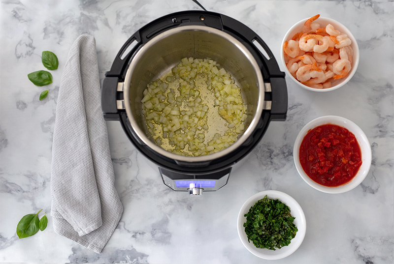 Onion sauteing in an Instant Pot with basil, diced tomatoes, and shrimp.