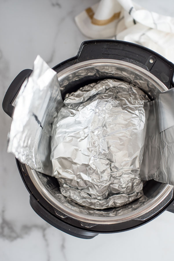 Overhead of spiral ham wrapped in aluminum foil inside an instant pot with a tin foil sling.