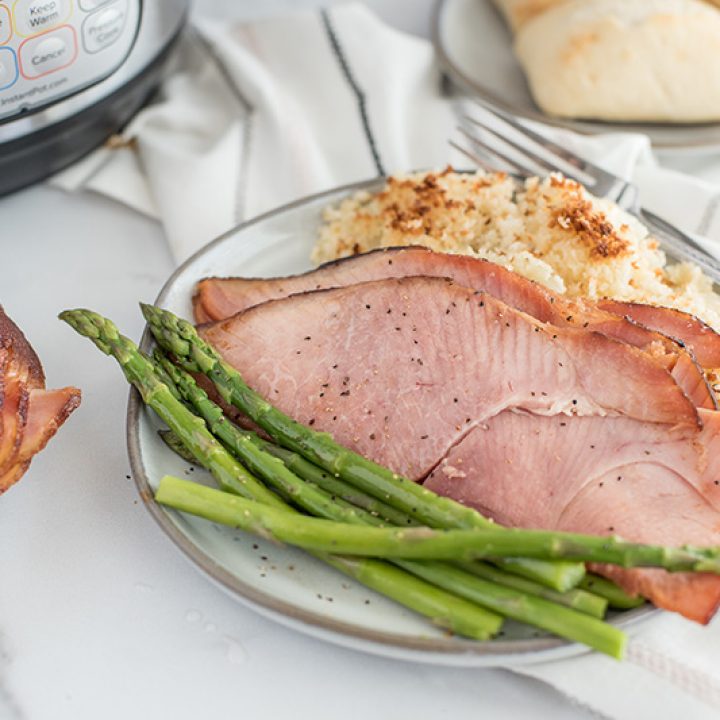 45 degree overhead of a plate filled with two large slices of Easter ham defrosted in the instant pot / pressure cooker, along with crisp asparagus, potato gratin and fresh rolls.
